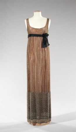 A peach colored evening dress decorated with rhinestones and a black waist tie.