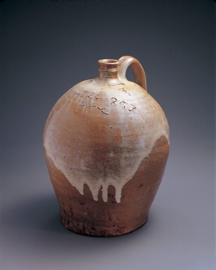 Photo of a fired clay-colored stoneware jug with a translucent coat of white glaze over its upper half.