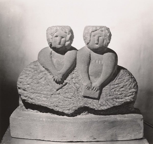 Rough sculpture of two women seated side by side, almost in bas relief. One woman is holding a book.