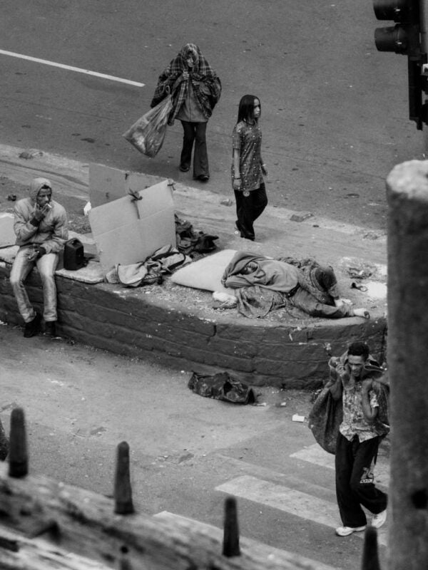 Photograph showing a street scene with presumed drug addicts walking, smoking, and sleeping.