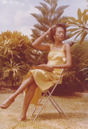 A photo of a seated woman posing in front of palm trees.
