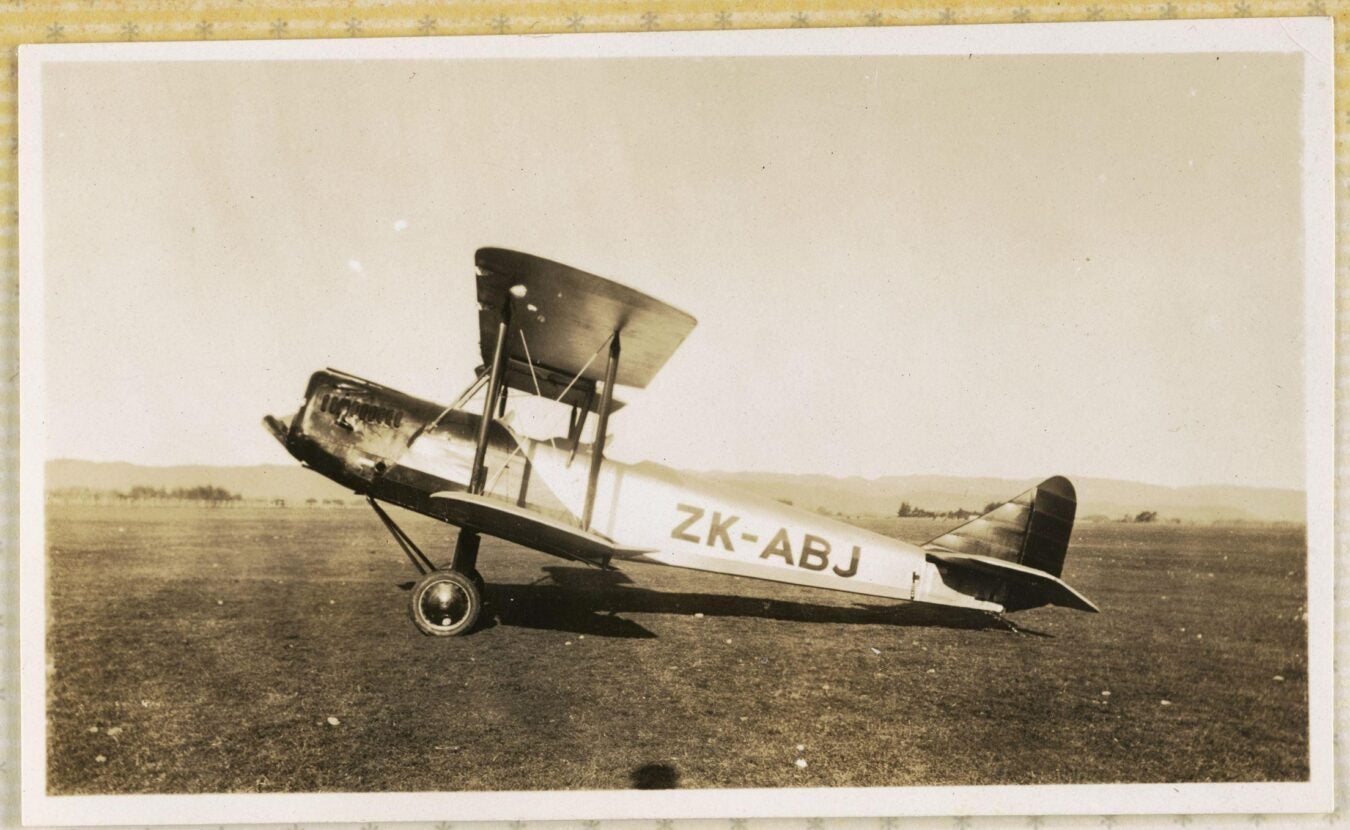A sepia-toned photograph of a parked biplane in a field. 