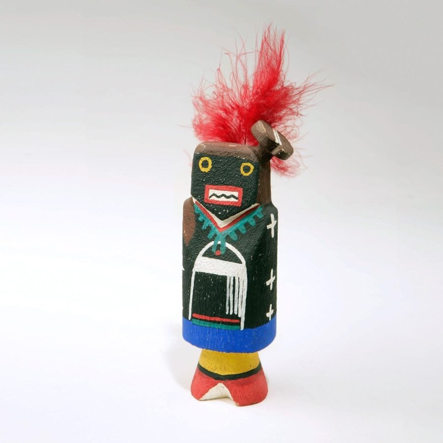 A small hand-painted wooden figurine with geometric features, bright colors, and a tuft of red feathers on top of its head.