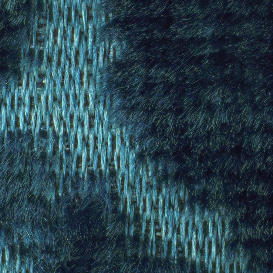 Close-up image of a textured blue fabric showing an interwoven pattern. The material has both smooth and fuzzy fibers, with lighter blue threads crossing darker blue areas, creating a soft, tactile surface with a woven appearance.
