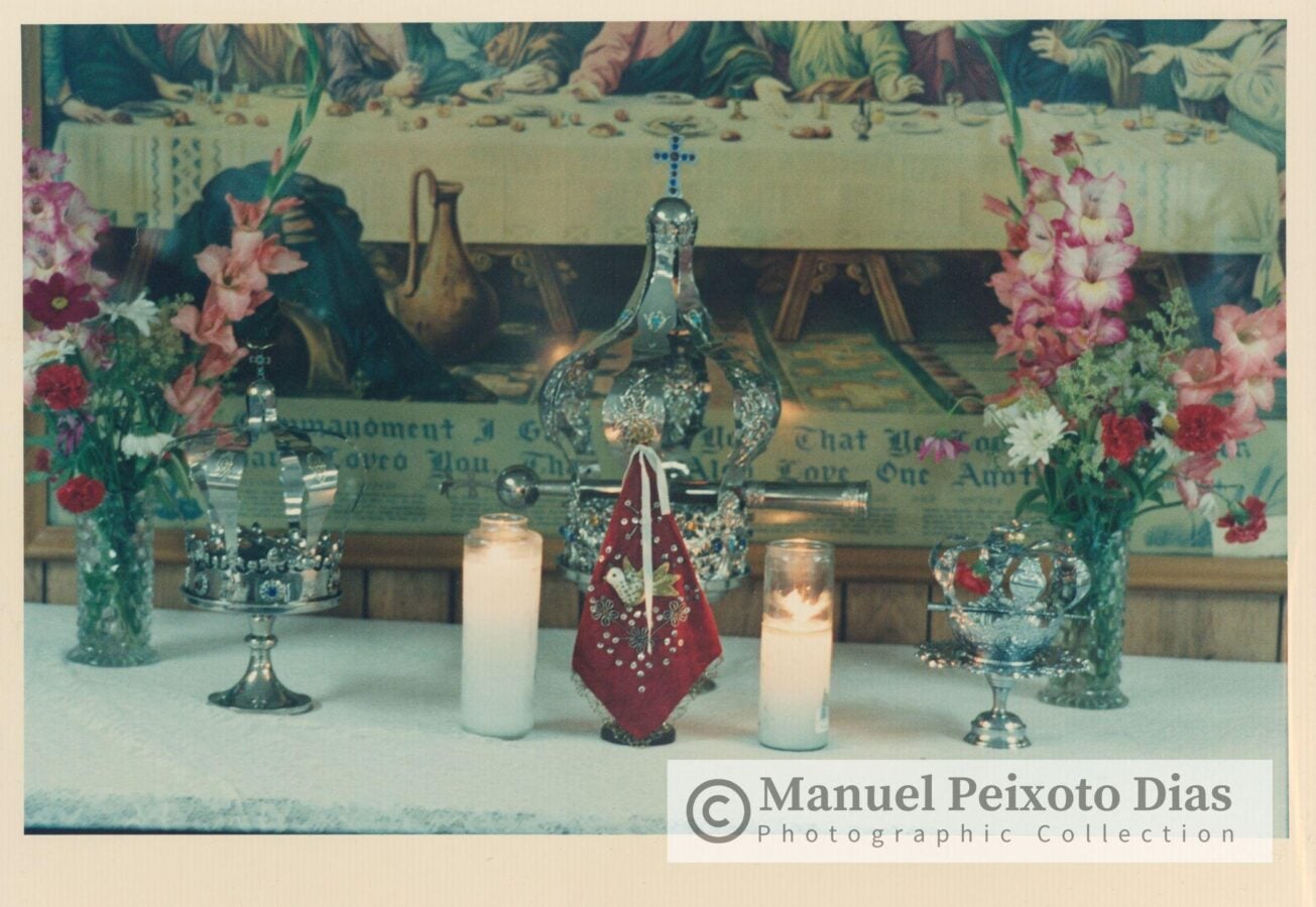 A decorated altar with candles, flowers, and ornate religious objects before a mural of the Last Supper.