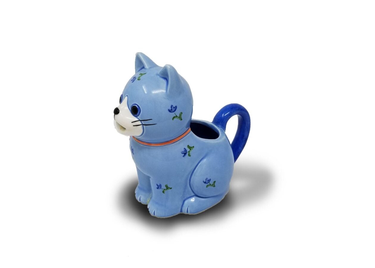 Small blue ceramic creamer shaped like a smiling cat with a tail handle and a spout opening on its back.