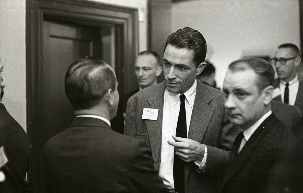Senator Claiborne Pell speaks with attendees at the Sea Grant Conference in 1965, surrounded by colleagues in suits and ties.