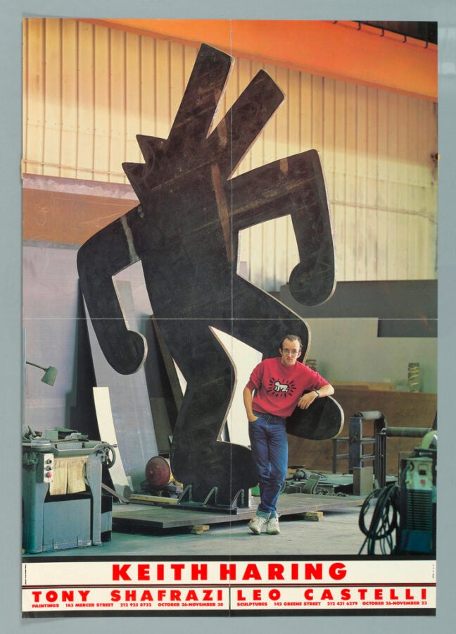 Artist Keith Haring stands in front of a large black sculpture of his signature figure in a warehouse space, with bold red text promoting his 1985 Tony Shafrazi and Leo Castelli Gallery exhibitions.