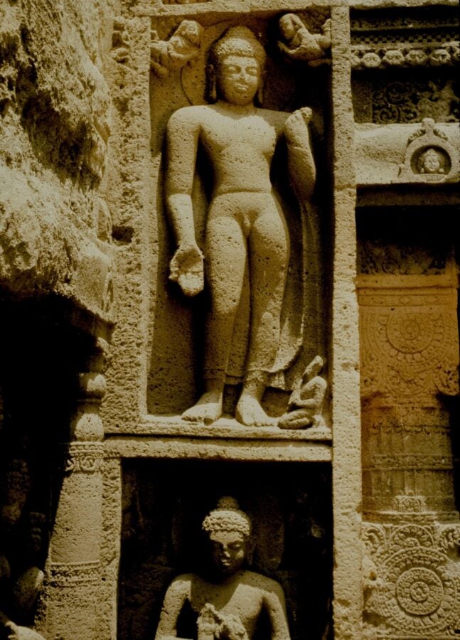 Carved stone sculptures at the Ajanta caves in India depicting standing and seated Buddha figures within elaborately detailed niches.