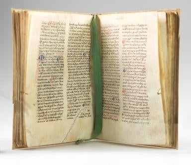 Open medieval manuscript showing two pages of Latin text written in dense columns with red and blue initials and a green ribbon bookmark.