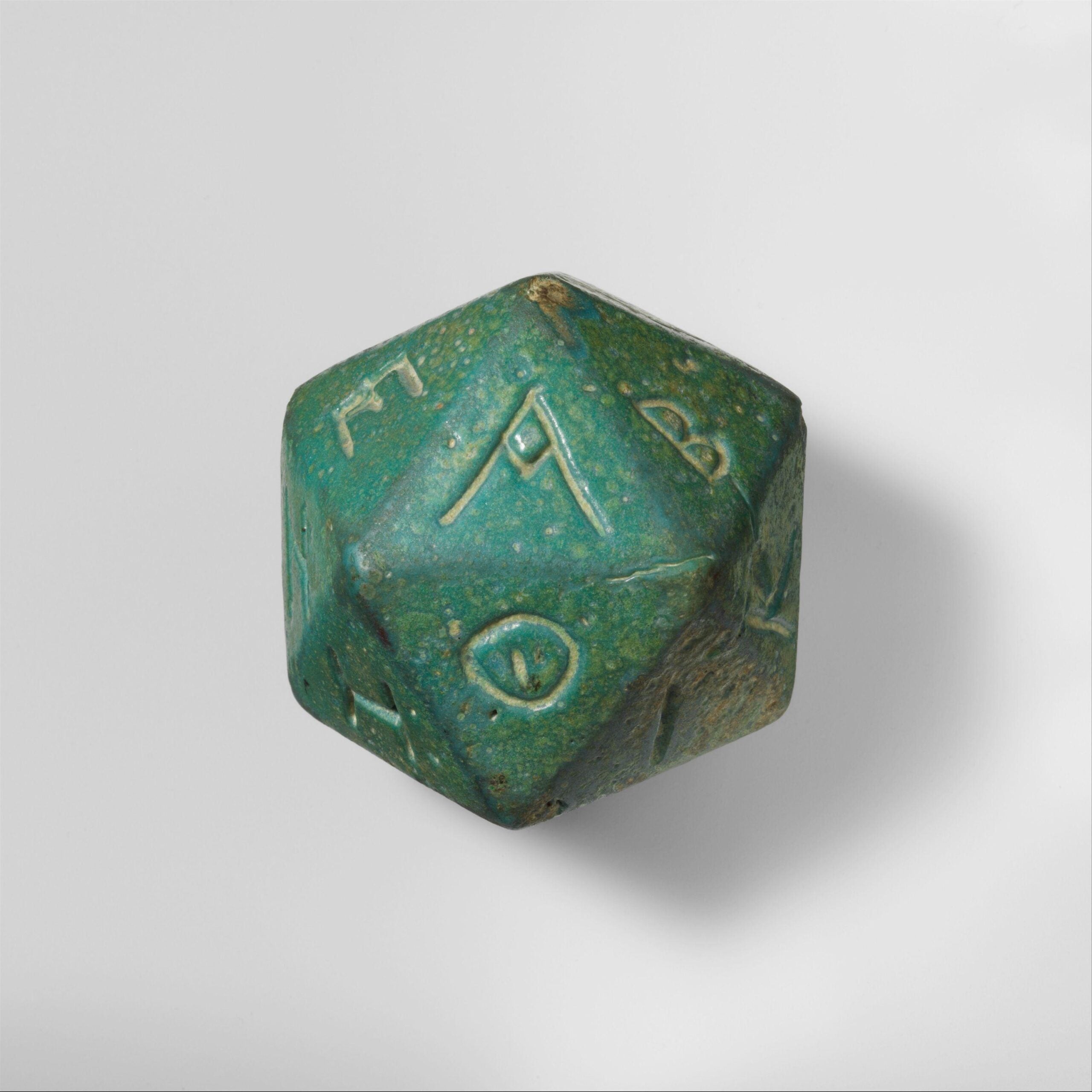 A faience polyhedron inscribed with letters of the Greek alphabet, dating to the 2nd or 3rd century CE. The object is a vibrant green-blue color and features inscriptions on each of its faces, showcasing the geometric precision and cultural significance of the artifact.