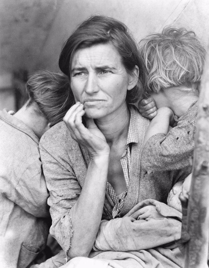 A black-and-white portrait of Florence Owens Thompson, a migrant mother during the Great Depression. She gazes into the distance with a worried expression, as two of her children lean on her shoulders and a baby rests in her lap. Her tattered clothing and lined face emphasize the economic struggles of the era.