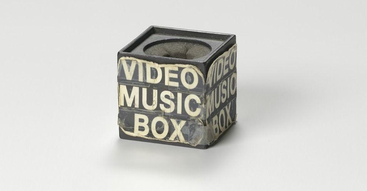 A black microphone box used on the television show Video Music Box, featuring white text wrapped around it that reads “Video Music Box” in a bold, graphic style. The box shows signs of wear and tear, reflecting its use. This microphone box, dating back to around 1988, is part of the collection at the Smithsonian National Museum of African American History and Culture.