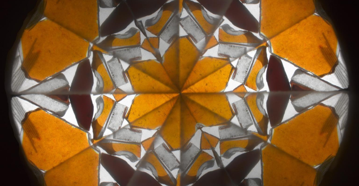 View through Brewster’s Patent Kaleidoscope, showing a symmetrical geometric pattern of orange, white, and black triangular shapes forming a star-like design.