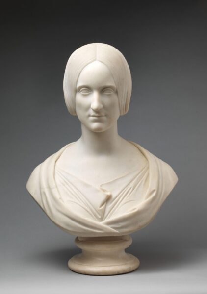 A marble bust of a woman with smooth features and a center-parted hairstyle, wearing a draped gown; displayed against a neutral gray background.