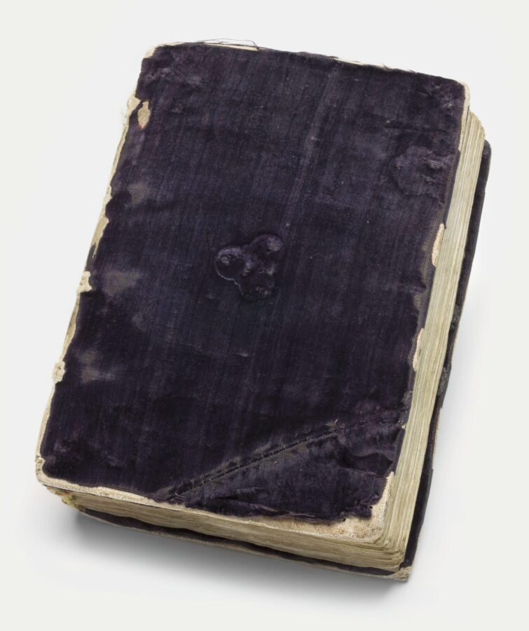 Worn velvet binding of a 15th-century Book of Hours, showing frayed edges and embossed decorative patterns.