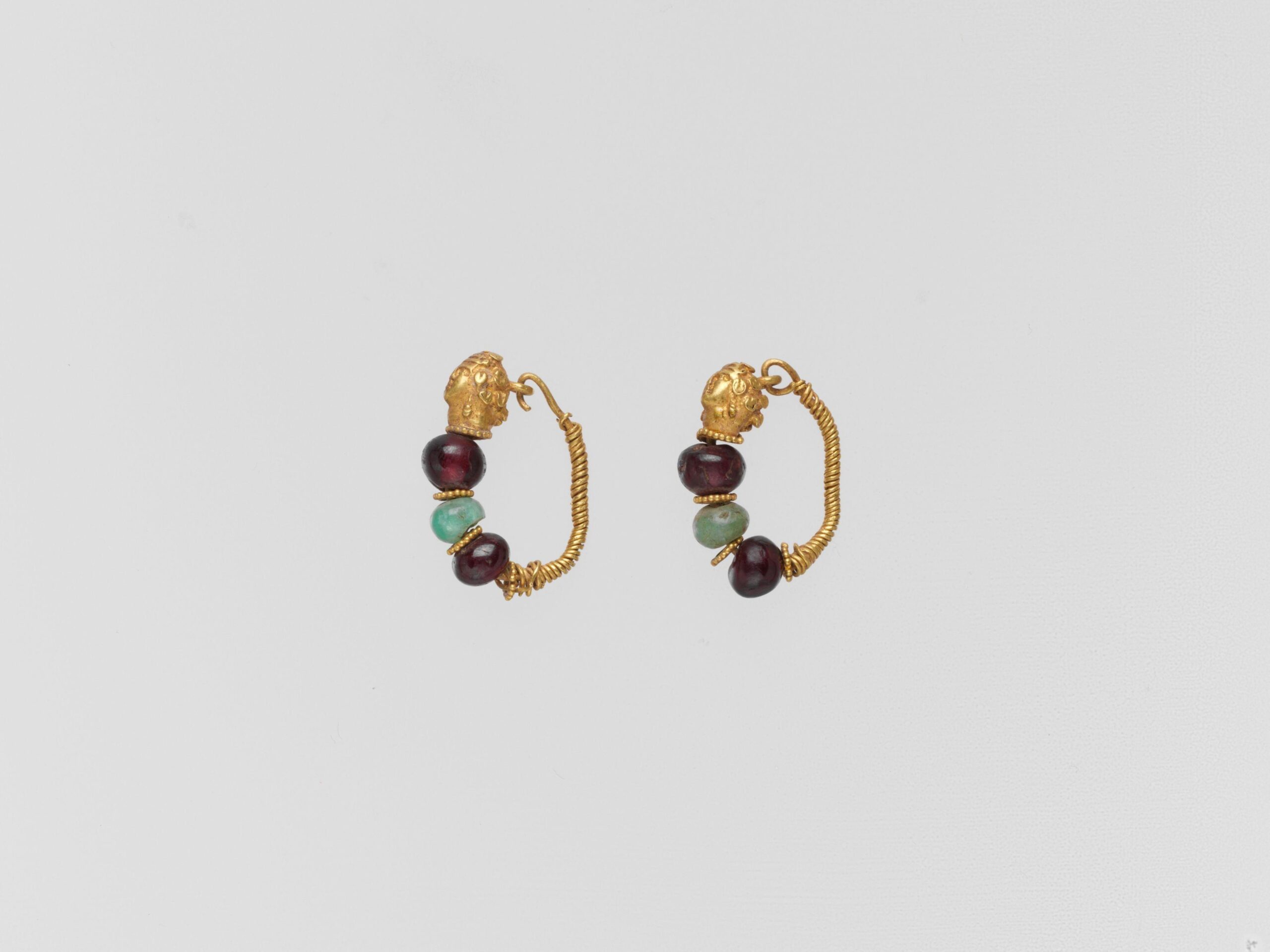 A pair of 2nd-century BCE Greek gold earrings featuring lion-head terminals and wire hoops adorned with red garnet and green glass beads.