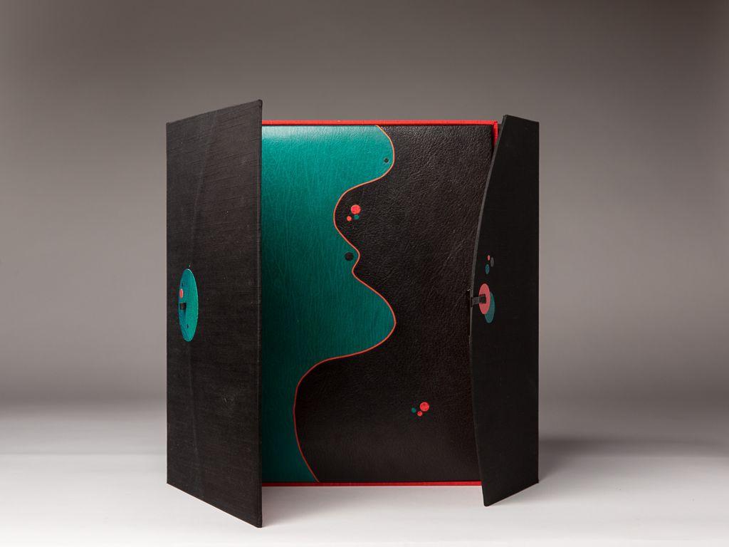 A contemporary artist’s book with black covers that open to reveal a teal and black abstract design resembling a profile silhouette, accented with red and teal dots.
