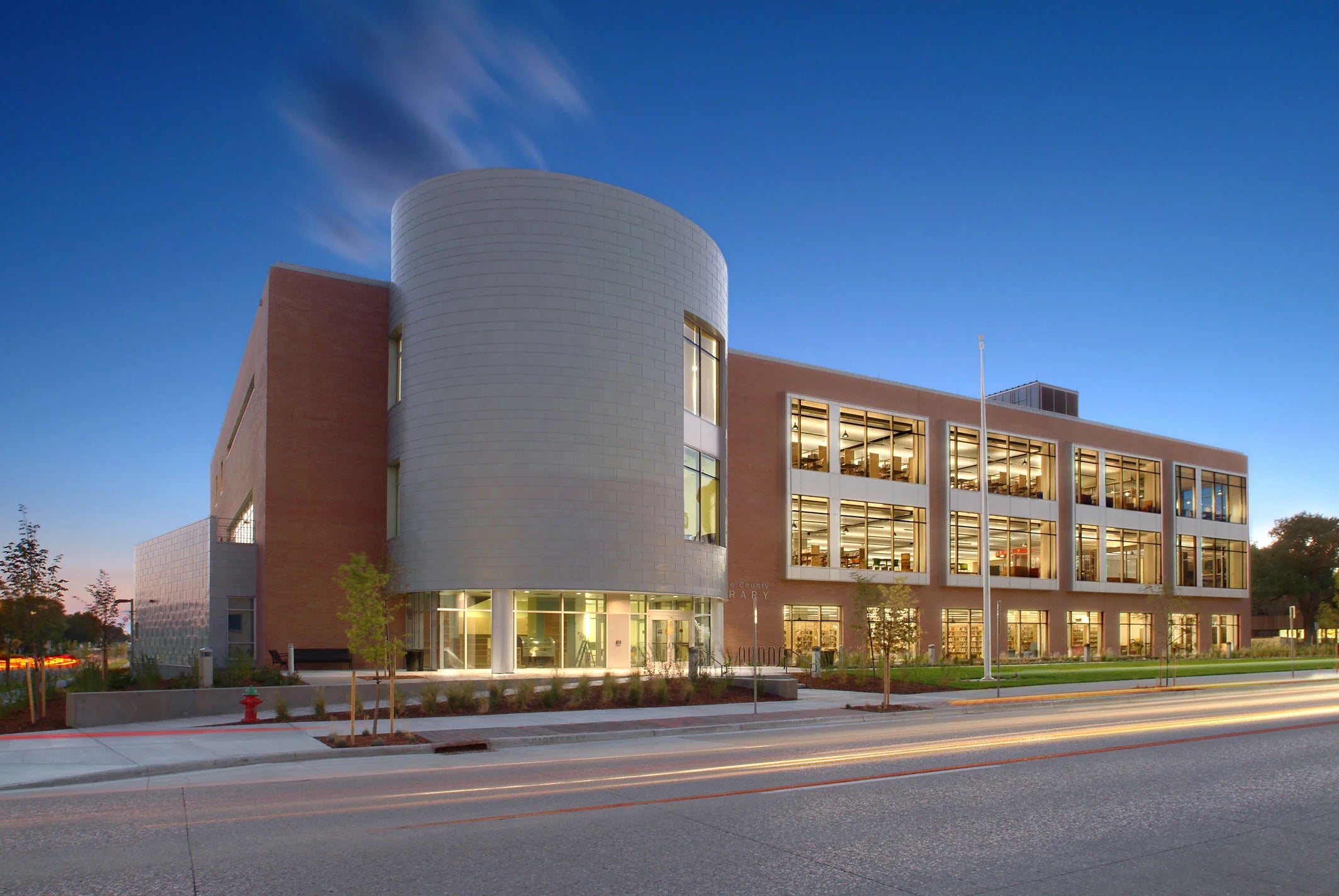 Exterior view of the library’s rounded metal and brick facade illuminated at twilight, with light trails from passing cars.