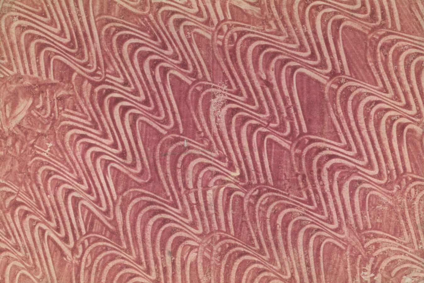 Close-up of a red marbled book cover featuring a repeating wavy line pattern in lighter and darker shades of red.