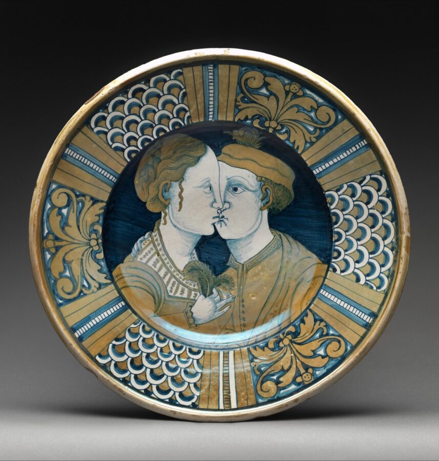 Decorative ceramic plate painted with two figures in profile kissing, framed by gold and blue patterns and motifs.