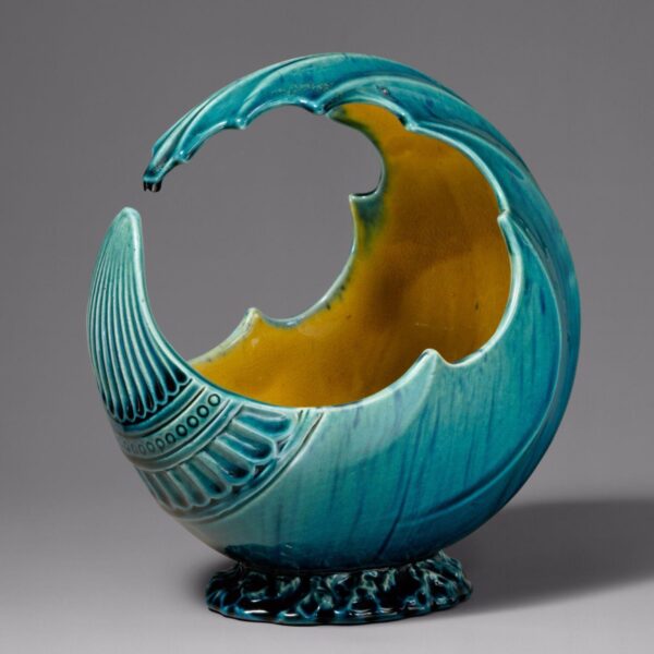 Decorative ceramic vessel shaped like a curling wave, glazed in turquoise blue with a yellow interior.
