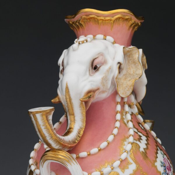 Decorative porcelain vase with pink and gold patterns, adorned with two white elephant heads forming the handles and embellished with pearls.