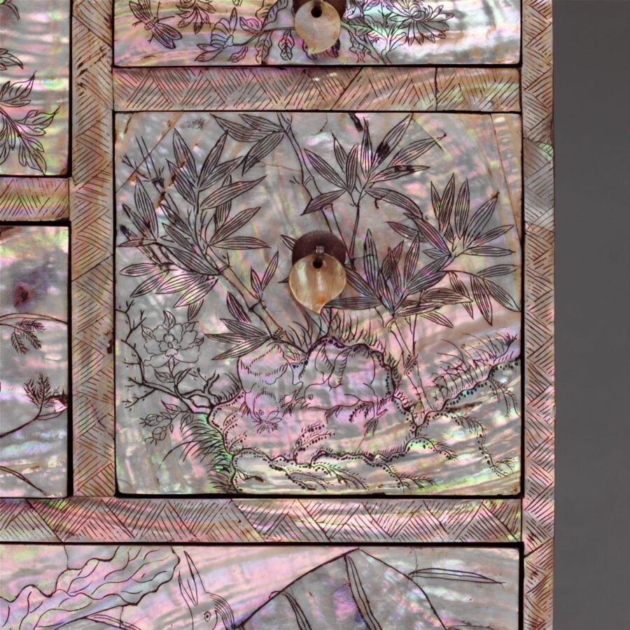 Close-up of a drawer panel showing engraved bamboo and floral designs on shimmering mother-of-pearl inlay with a round shell pull.
