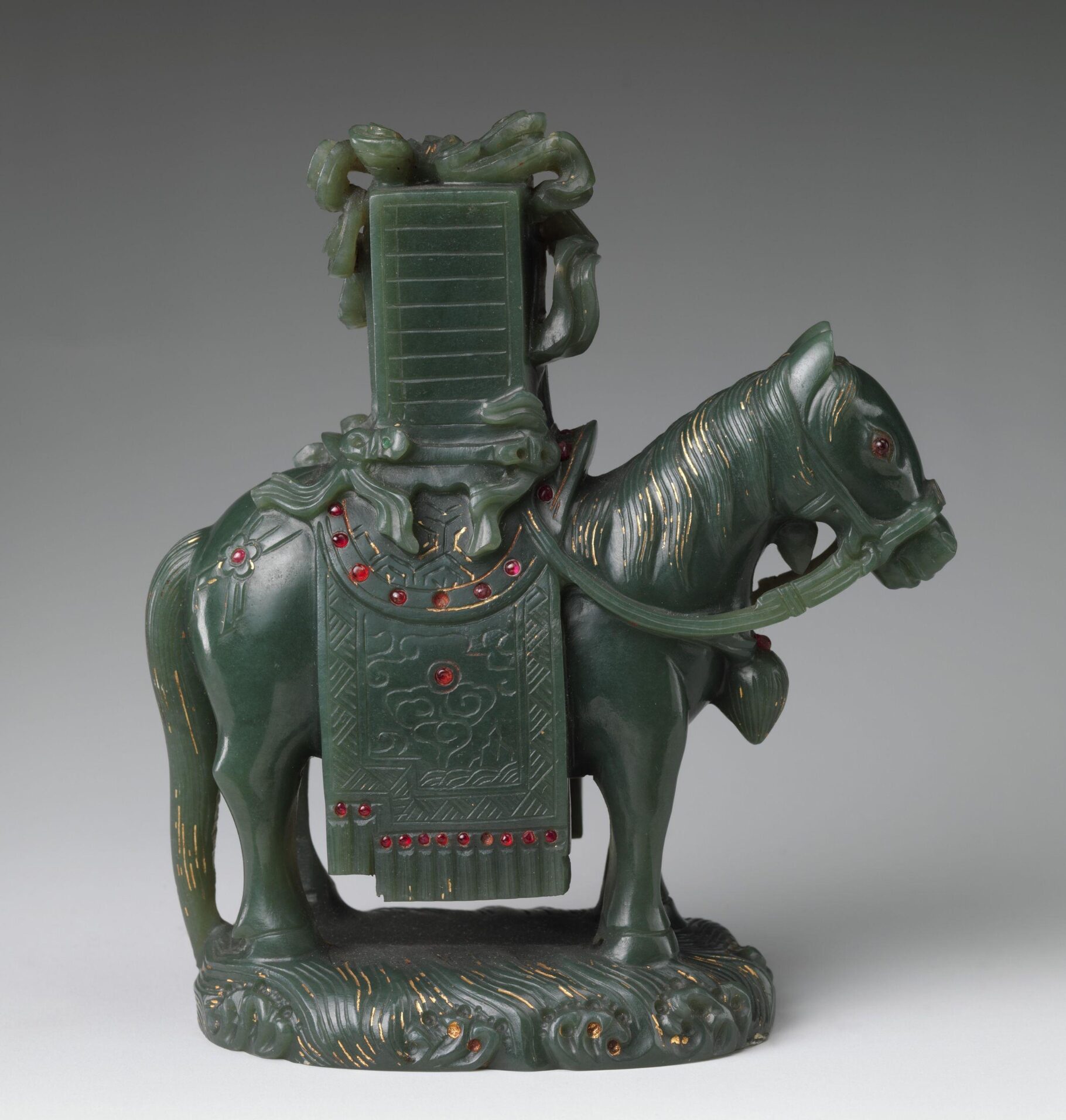 Carved jade figure of a saddled horse with intricate details, red gemstone inlays, and decorative gold accents.