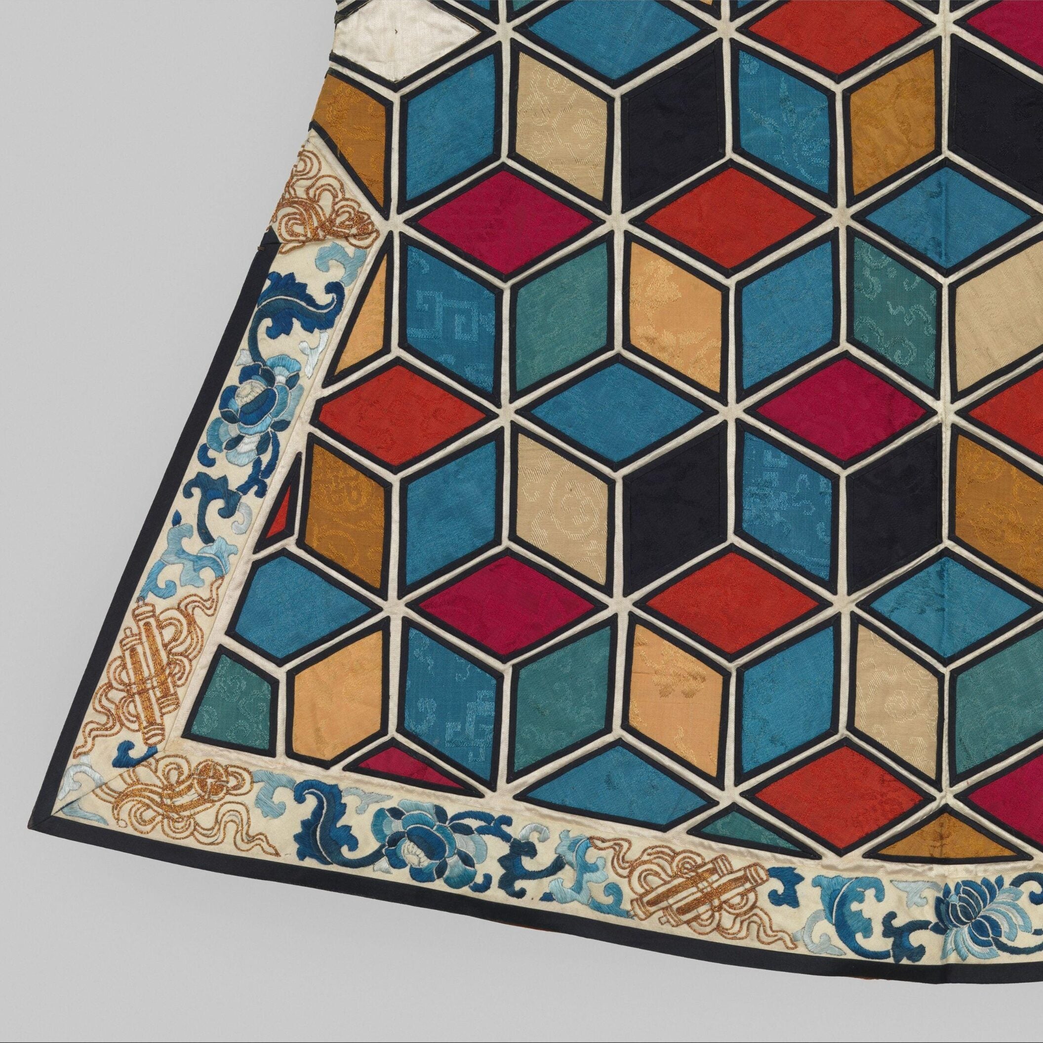 Detail of a textile with colorful, interlocking cube patterns bordered by blue floral and scroll designs.