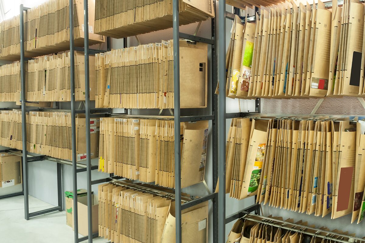 Rows of tall metal shelves filled with large brown archival folders organized in a storage room.
