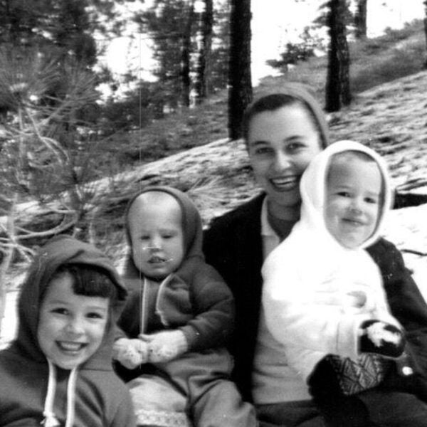 Black-and-white photo of a smiling woman outdoors with three young children dressed in hooded winter clothing.
