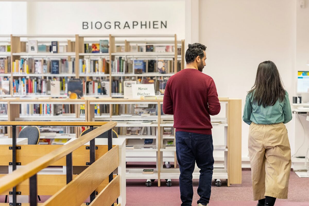 Two people walking and talking in a library aisle lined with bookshelves.