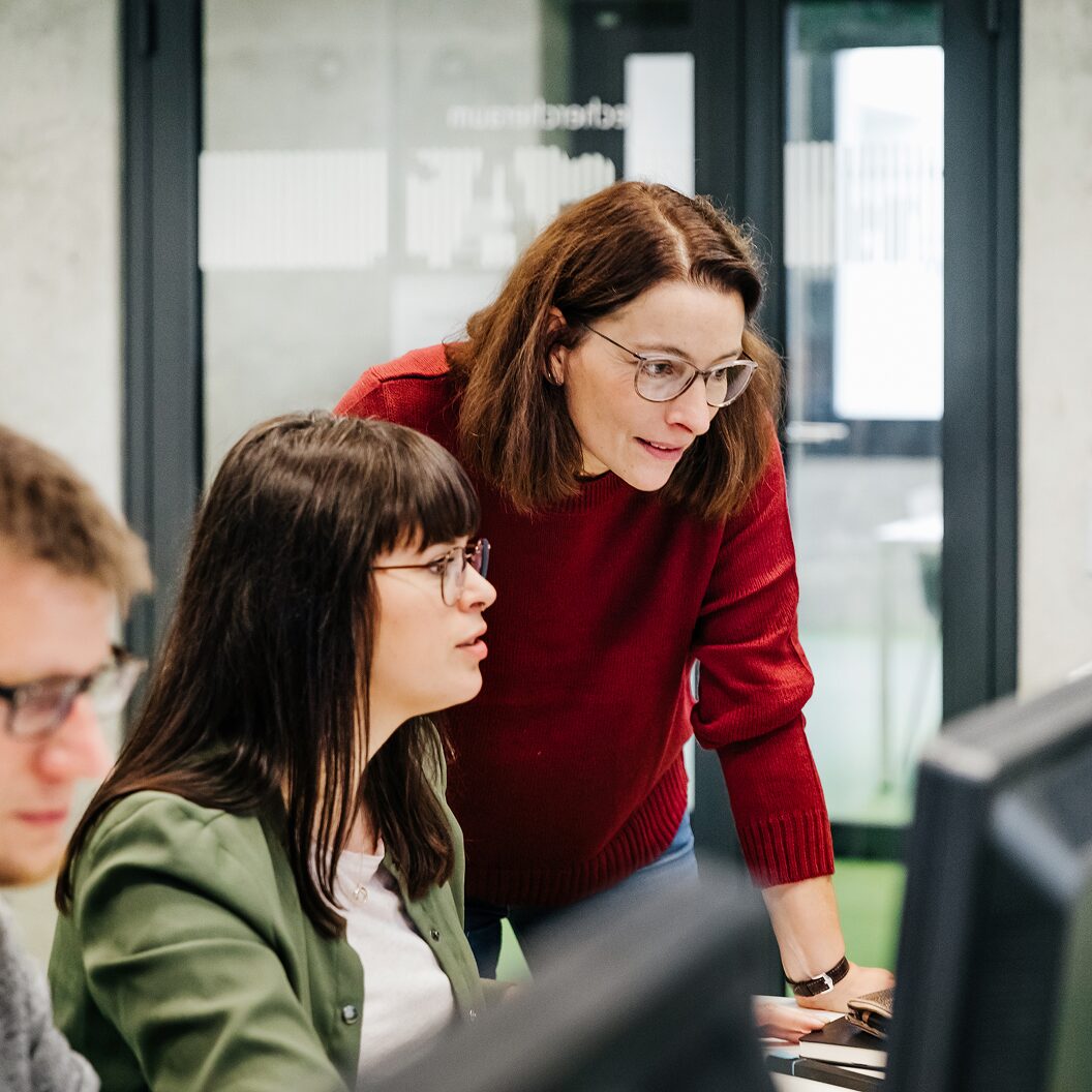 wo colleagues collaborating at a computer in a modern office, reviewing information on a screen together.
