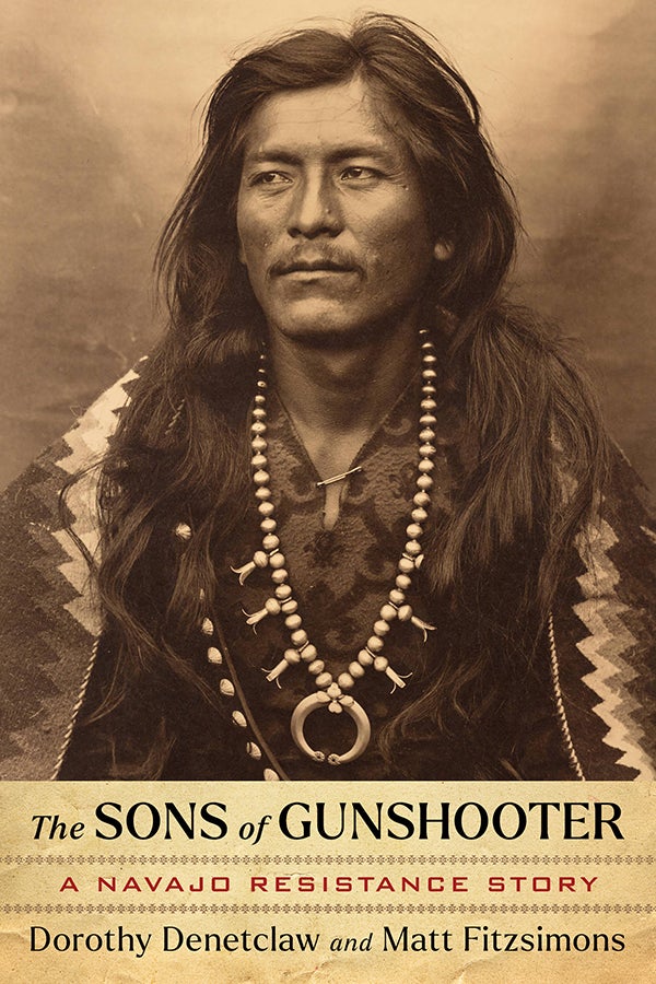 Sepia-toned portrait of a Navajo man wearing traditional jewelry and long hair over his shoulders. Text reads “The Sons of Gunshooter: A Navajo Resistance Story” by Dorothy Denetclaw and Matt Fitzsimons.