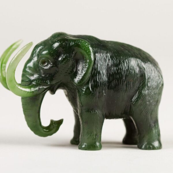 A small dark green carved figurine of an elephant with lighter green tusks and a curled trunk, shown against a plain light background.