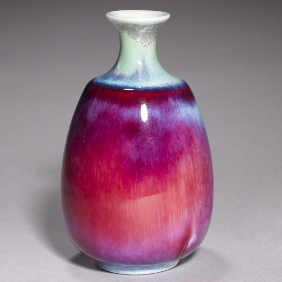 Small ceramic vase with a rounded body and narrow neck, glazed in gradients of deep purple, magenta, and blue against a gray background.