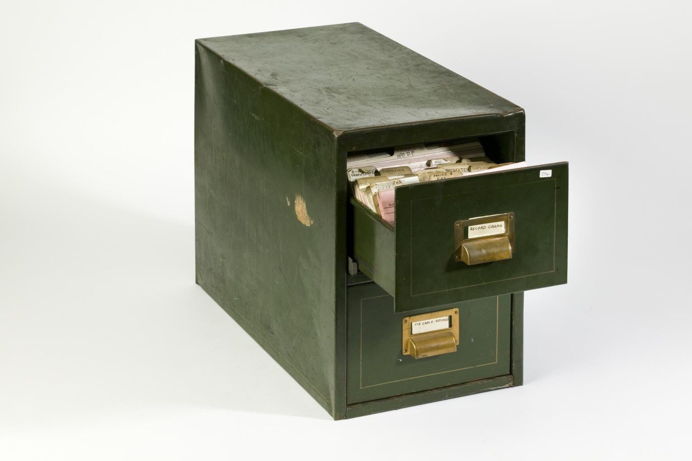 A dark green metal filing cabinet with two drawers, the top drawer open to reveal rows of labeled index cards.