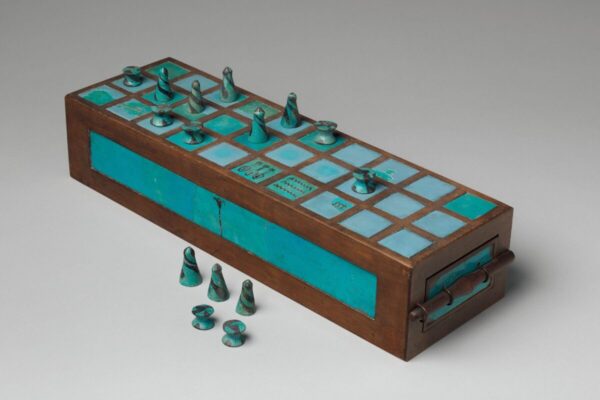 An ancient Egyptian game board made of wood and turquoise-colored inlays, with conical and spool-shaped playing pieces arranged on top and several pieces placed in front.