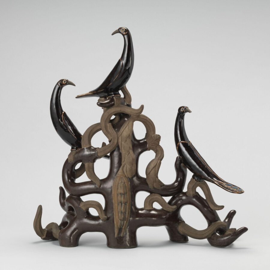 A sculpture featuring three sleek black birds perched on a twisting, tree-like form of interwoven organic shapes.