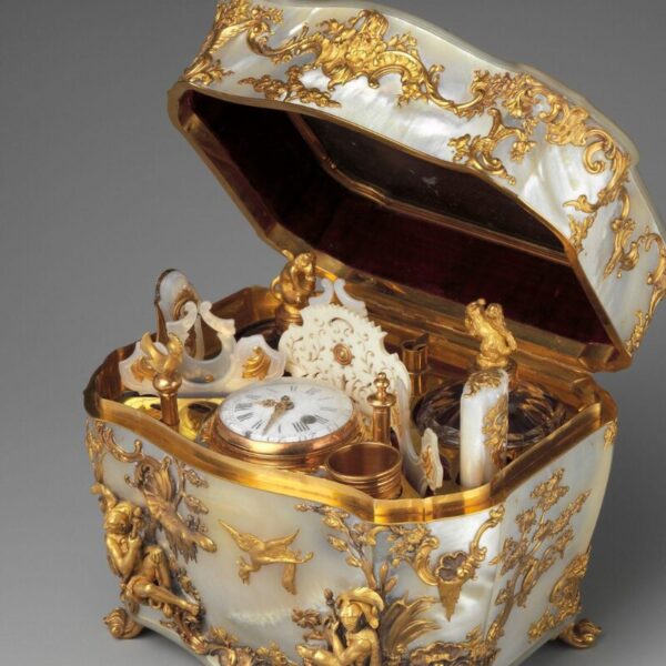 An ornate 18th-century nécessaire box with its lid open, featuring mother-of-pearl panels and elaborate gilded decoration. Inside are finely crafted grooming tools and a small clock, all set within a luxurious gold-trimmed interior.