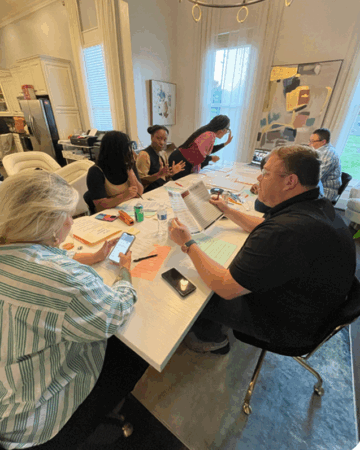 A wide lens shot of six people working around a large white table with flyers and pamphlets.