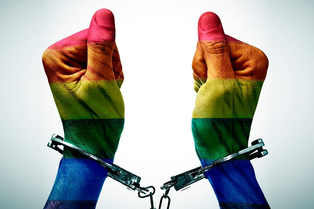 Pair of hands in handcuffs, overlaid with a rainbow flag gradient representing LGBTQ+ identity.