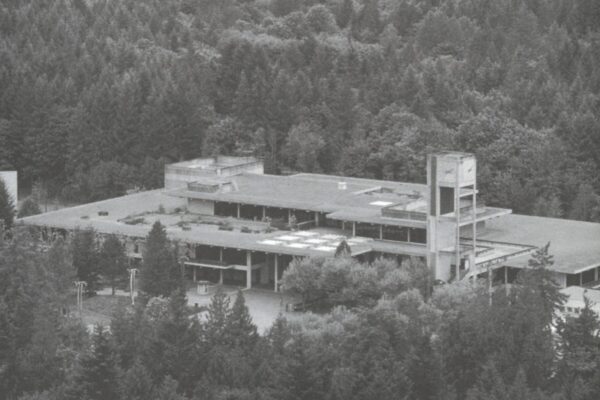 Black-and-white aerial photograph of The Evergreen State College campus surrounded by dense forest and hills.
