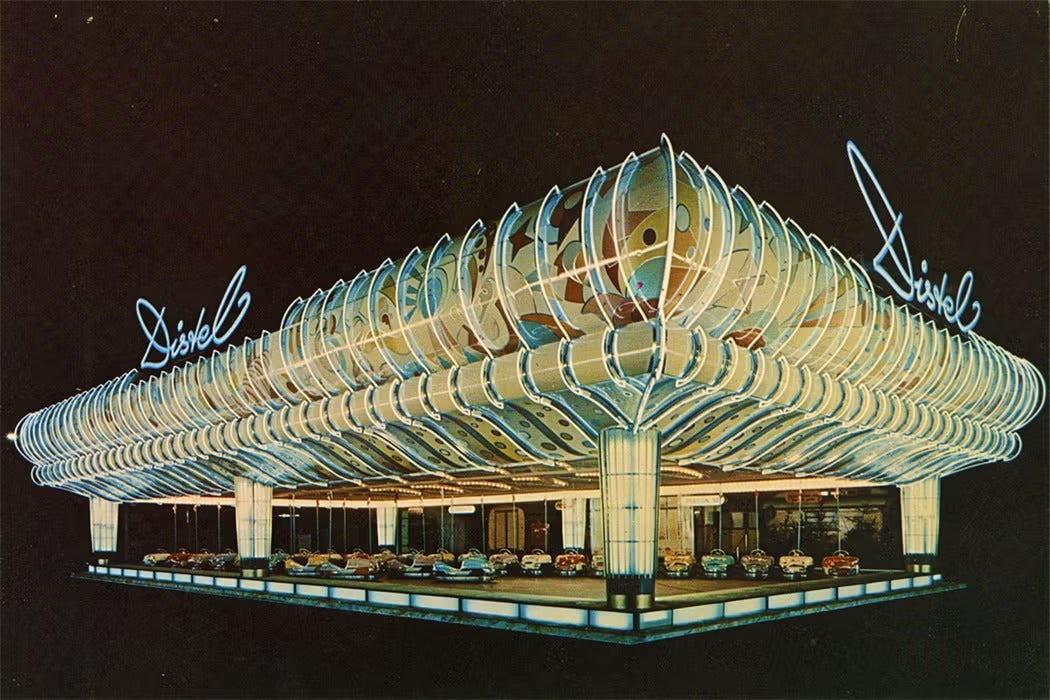 Nighttime rendering of the neon-lit “Skooter Building,” a mid-century amusement pavilion with a sweeping, futuristic canopy outlined in blue and white lights. The structure features stylized, atomic-age patterns and glowing columns, with bumper cars visible beneath the illuminated roof.