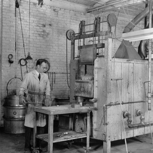 Black-and-white photograph of a man operating industrial machinery in a workshop.