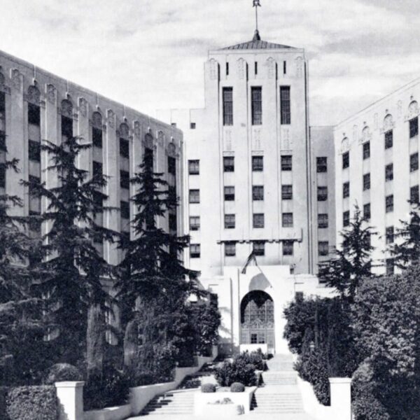 Black-and-white photograph of a large institutional building with a central tower and landscaped walkway.
