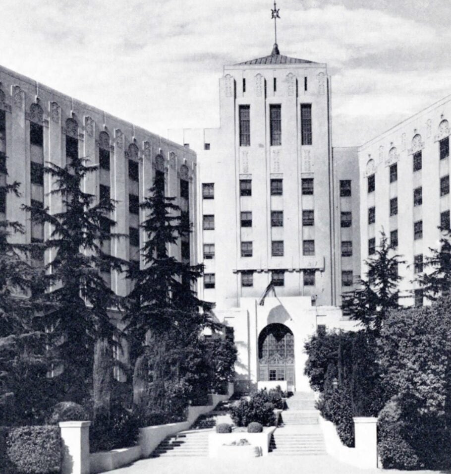 Black-and-white photograph of a large institutional building with a central tower and landscaped walkway.