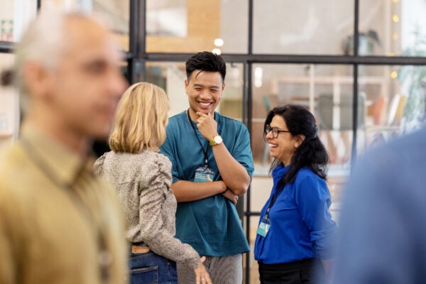 Three professionals wearing conference badges chatting and smiling in a modern office or event space.