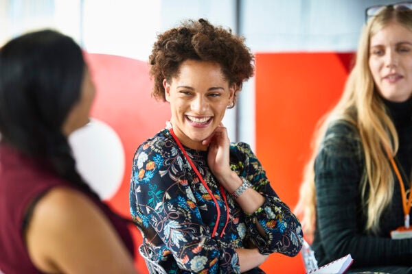 Woman smiling and participating in a group discussion, wearing a patterned blouse and conference badge.